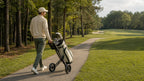 Golfer pulling a two-wheel golf trolley with a secured golf bag along a fairway path