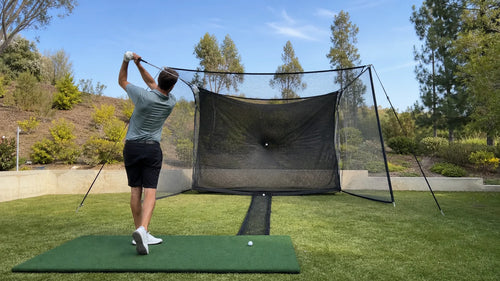 Golfer hitting into a practice net with side barriers and a lower ball-return channel